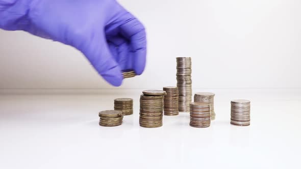 A hand in medical gloves puts coins into a column. Investment concept alt