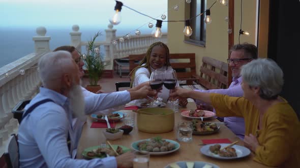 Happy multiracial seniors toasting with red wine glasses together on house patio dinner