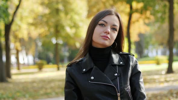 Portrait of Beautiful Woman Wearing Black Leather Jacket Walk in the Autumn Park, Looking at Camera alt