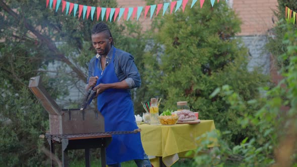 Focused Man in Apron Blowing Smoke on Barbecue Grill Outdoors alt