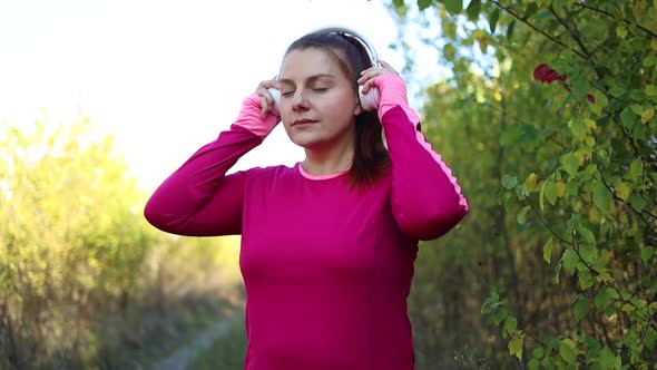 Young Active Sports Girl in Workout Clothes Puts on Wireless Headphones to Start Running in the City