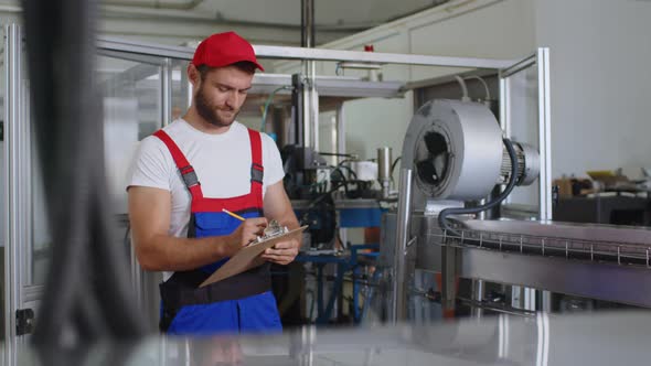 Young Factory Man in Uniform Making Notes on Clipboard at Water Production Factory