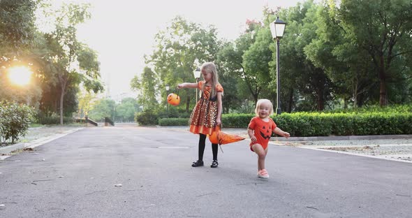 Cute Little Caucasian Kids with Blonde Hair Seven Years Old in Costume of Witch with Hat and Baby alt