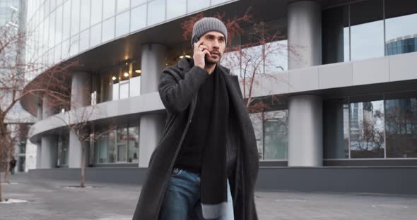 Young Man Talking By Phone While Walking in the Street Near Business Center