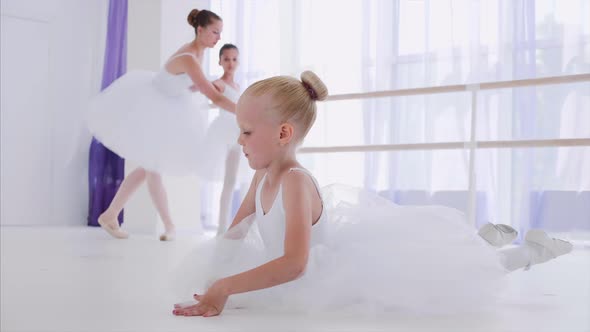 Child Girl Ballerina in White Tutu is Doing Stretch Exercises on Ballet Lesson alt