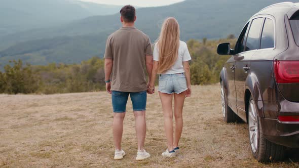Young Traveler Couple on Road Trip in Mountains Standing Near Car