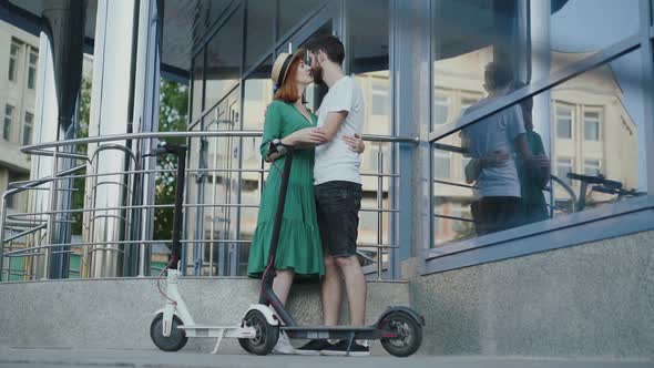 Couple in Love Embraces and Kisses Each Other at Office Centre Near Scooters alt