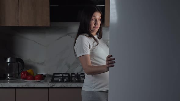 Pregnant Brunette Woman Eats Greenery in Kitchen at Night alt