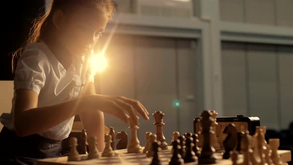 Beautiful girl child playing chess, making a move piece and presses the key of the chess clock