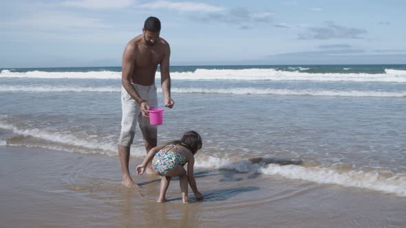 Little Girl and Her Dad Picking Shells Into Bucket alt