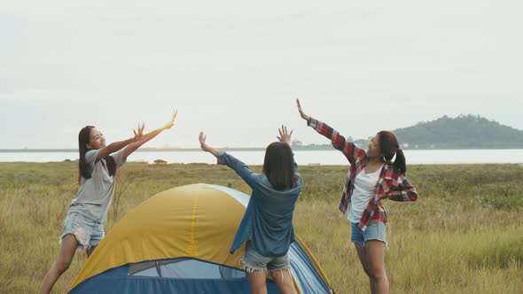 Group of a young Asian women camping pitch a tent while sunset enjoying having fun together a summer