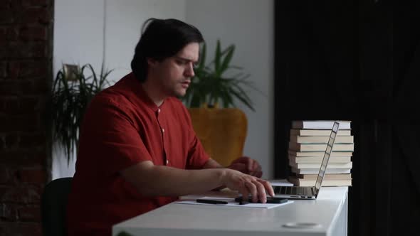 Man working at home office at laptop and talking by mobile phone alt