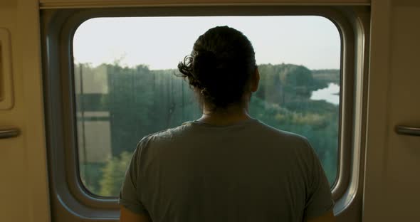 Young Attractive Tourist Looker Out of the Window of a Moving Train at Sunset alt