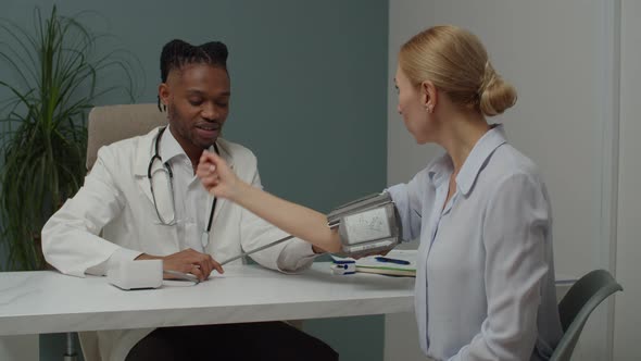 Male Doctor Examining Woman Patient By Checking Blood Pressure Indoors alt