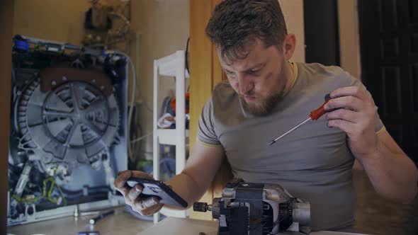 A Man Fixes a Washing Machine and Watches Instructions on His Phone