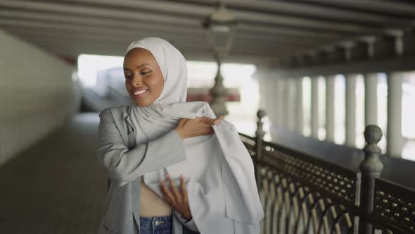 Smiling Black Woman Wraps Shoulder with Hijab on Waterfront alt