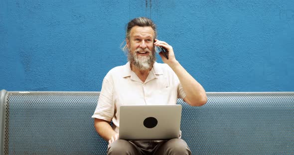 Senior Man Working with Laptop and Talking on the Phone in the Street alt