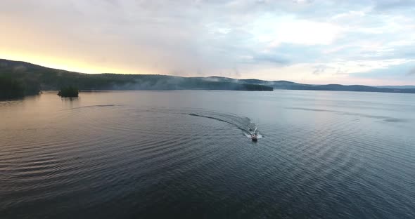 Motor boat floats across the lake at sunset aerial view