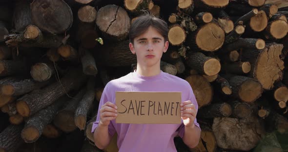 Ecology Concept - Save the Planet Poster. Activist Holding Poster on the Background of Felled Trees alt