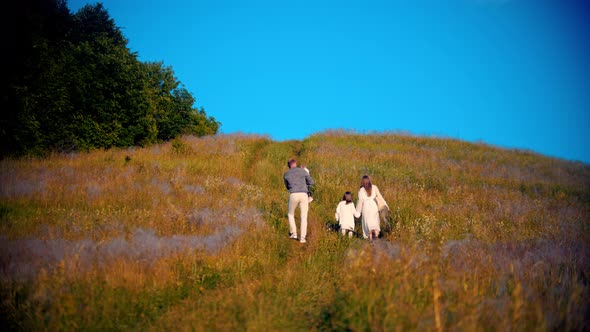 Young Family Walking Upwards on the Field on Early Sunset alt