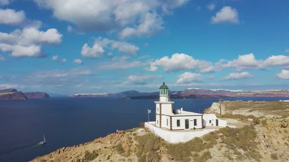 4k aerial drone orbit flying around beautiful lighthouse Santorini Greece with blue sky and clouds alt