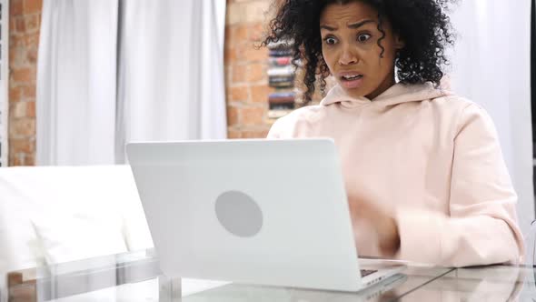 AfroAmerican Woman Sitting on Couch Upset By Loss Working on Laptop alt