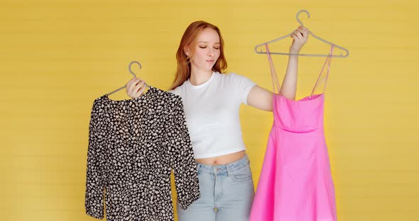 A young woman chooses clothes on yellow background. Hard choice  alt