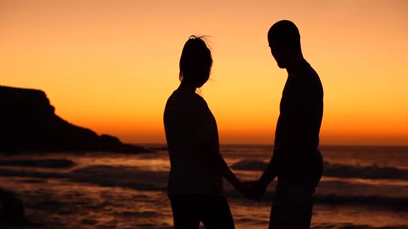 Couple making a silhouette heart shape with hands at seaside at sunset in Fue