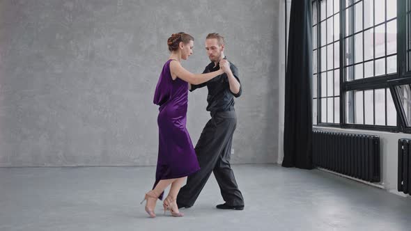 Man and Woman are Sensually Dancing a Tango in a Grey Studio with Large Windows alt