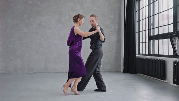 Man and Woman are Sensually Dancing a Tango in a Grey Studio with Large Windows