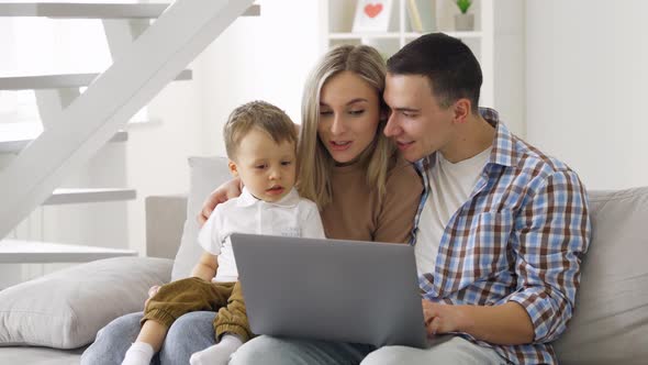 Happy Young Couple with Kid Sitting on Couch at Home Laptop Talking to Parents alt