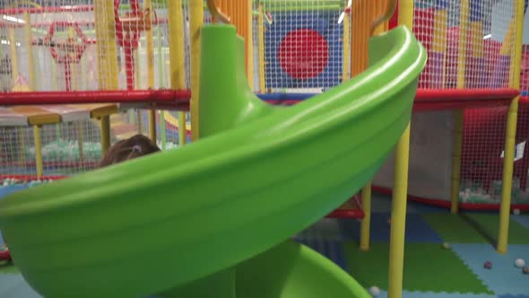 Happy Little Girl Moving Down on Slide in Children's Play Center