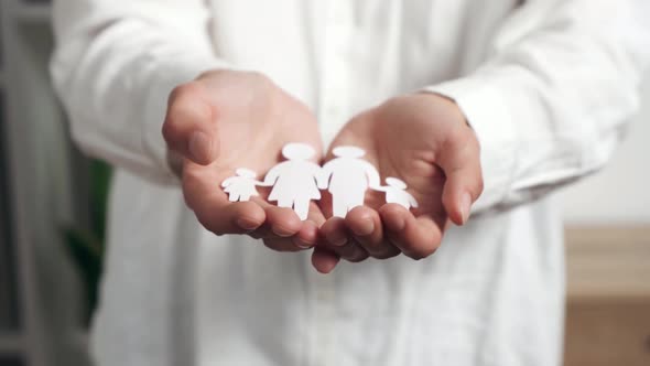 Close Up Female Hands Hold A Young Family Cut Out Of A Paper Sheet, A Symbol Of Well Being alt