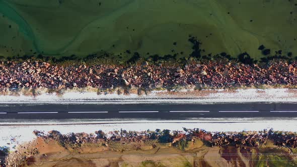 Aerial Vertical Drone Shot of straight empty asphalt road along rocky sea shore.	