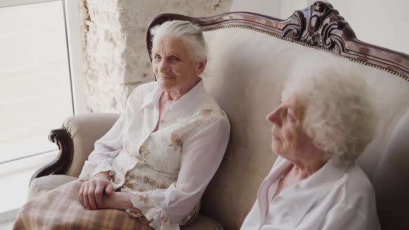 Two Elegant Grandmothers Sitting on a Sofa and Having Pleasant Time in Room alt