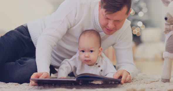 Happy Father and Little Son are Reading a Book with Fairy Tales By the New Year Tree alt