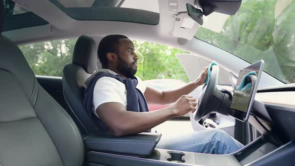 Bearded Black-Skinned Man which Sitting Inside Own Car and Wiping Handlebar and Navigator Screen alt