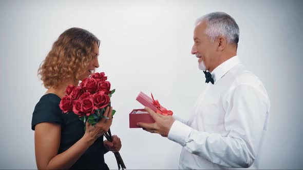 A Caring Middleaged Husband in Love Gives a Gift in a Gift Box to a Beautiful Happy Wife for