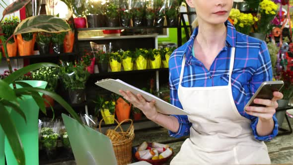 Female florist using mobile phone in flower shop alt