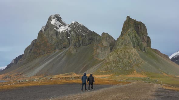People Walking Over Black Sand Beach And Gravel To Dramatic Mountains alt