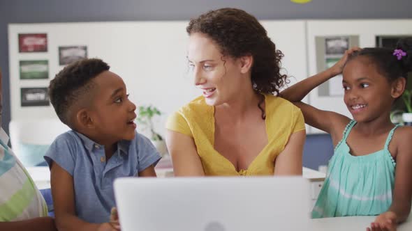 Video of happy caucasian female teacher and african american pupils using laptop alt