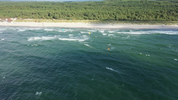AERIAL: Pan Tracking Shot of Surfers Near the Sandy Beach on a Bright Day 