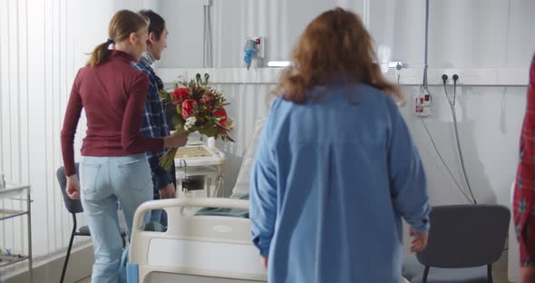 Group of Friends Visiting Sick Young Man in Hospital and Bringing Flowers alt