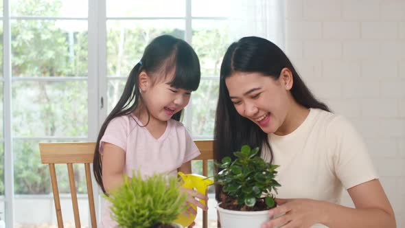 Asian family mom and daughter watering plant in gardening near window at house. alt