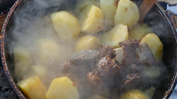 A Cook Stirs Potatoes With Beef Ribs With Wooden Spoon in a Cauldron