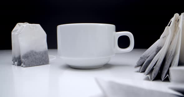 Super Closeup Set of Tea Bags on a White Table on a Black Background and a White Cup of Tea alt
