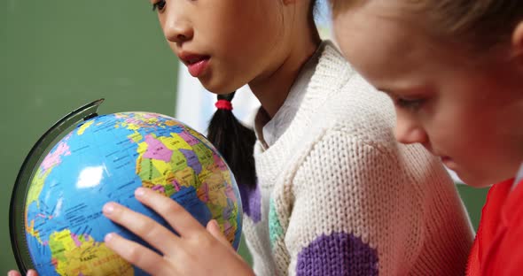 School kids looking at globe in classroom at school alt