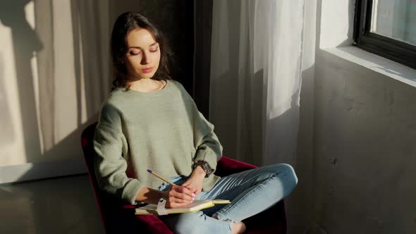 Beautiful Woman Sitting Near Window and Writing Things at the Sunset alt