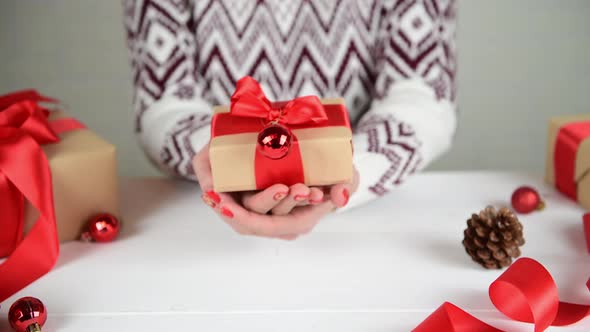 Female hands showing wrapped present in kraft paper box with red ribbon bow alt