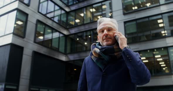 A Grayhaired Man Uses a Mobile Phone Standing in Business Center of the City alt